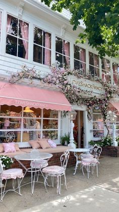 the outside of a restaurant with tables and chairs in front of it that has pink flowers growing on the windows