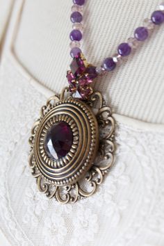 "A lovely deep purple Gay Nineties antique button from the late 1800's forms the centerpiece of this elegantly simple, but statement,t necklace. The button rests on a slightly larger bit of filigree. The amethyst beads are the perfect complement and the purple earring fragment sitting just above the button is the perfect finishing touch. The color of the stone is quite deep. Picture 5 shows a bit of the color coming through. This necklace is adjustable between 18\" - 23\". I work with antique an Antique Round Purple Necklace, Vintage Purple Round Pendant Jewelry, Vintage Purple Pendant Necklace, Vintage Purple Round Pendant Necklace, Vintage Round Purple Necklace, Vintage Purple Round Necklace, Deep Picture, Purple Earring, Vintage Assemblage