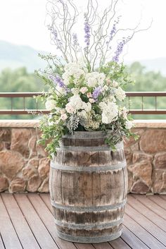 a wooden barrel filled with flowers on top of a wooden floor next to a stone wall