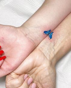 two hands holding each other with red nail polish on them and a blue butterfly tattoo