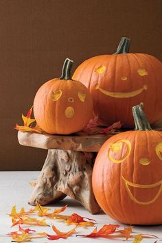 three pumpkins with faces painted on them are sitting on a wooden stand surrounded by leaves