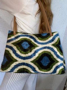 a woman is holding a purse with blue and green designs on it's side