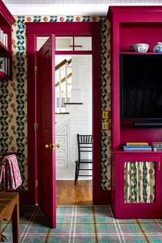 an open door leading to a living room with red painted walls and colorful wallpaper