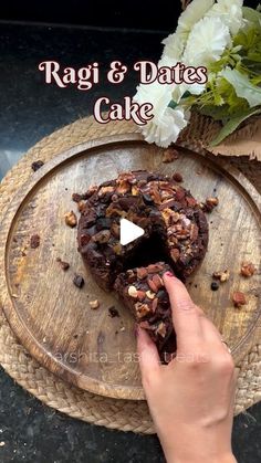 a person holding a piece of cake on top of a wooden tray with flowers in the background