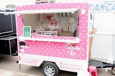 a pink and white food truck parked next to a wall with writing on the side