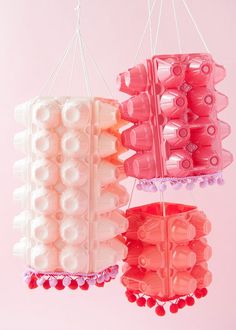 two plastic objects hanging from strings on a pink background, one with red beads and the other white