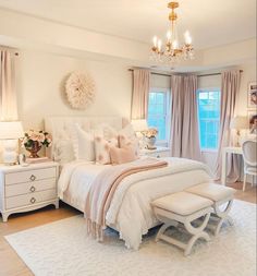 a white bedroom with chandelier, bed and dressers in the corner area