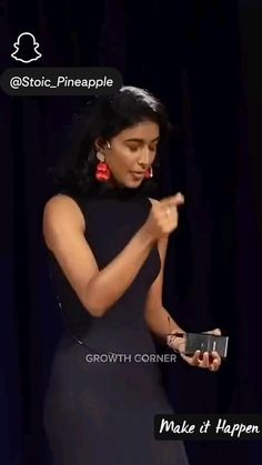 a woman in a black dress holding a cell phone and pointing to the screen with her right hand