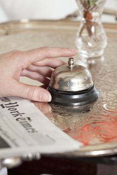 a person's hand is on top of a silver tray with a small bell