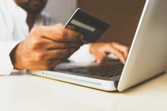 a man holding a credit card while using a laptop