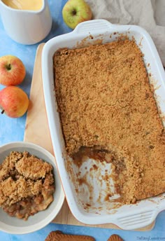 an apple crumbler cake in a white dish next to some apples