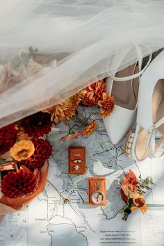 wedding shoes and bouquets on a map with the bride's veil blowing in the wind