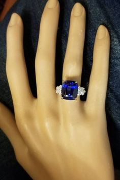 a hand with a ring on it that has a blue stone in the middle and two white diamonds at the bottom