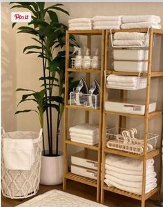 a shelf filled with lots of white towels next to a potted plant and basket