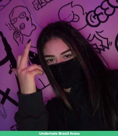 a woman wearing a black face mask and making the v sign with her hand while standing in front of graffiti covered wall