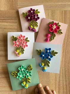 four different colored paper flowers are on the table and someone is holding their hand out to them