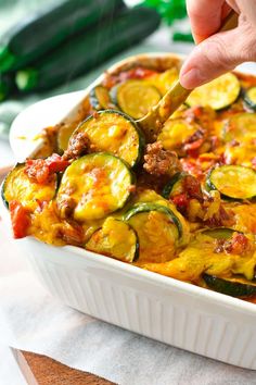 a person is spooning some food out of a casserole dish with zucchini