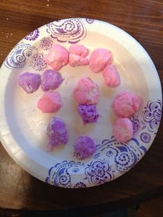 purple and pink rocks are on a white plate with blue designs around it, sitting on a wooden table