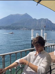 a person sitting on a bench by the water with mountains in the background and a boat out to sea