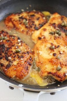 three pieces of chicken cooking in a skillet on the stove with some seasoning