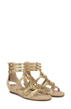 A tapered woven wedge lofts a strappy sandal designed with glitzy beaded accents that are perfect for a vacation look. 1" heel (size 8.5) 4" ankle shaft Back zip closure Adjustable ankle straps with buckle closures Synthetic and textile upper/synthetic lining/rubber sole Imported Gold Low Heel Sandals For Summer, Embellished Synthetic Toe Post Sandals, Gold Embellished Toe Post Sandals, Beach Wedge Sandals With Heel Strap And Low Heel, Beaded Open Toe Synthetic Sandals, Beaded Synthetic Open Toe Sandals, Gold Toe Post Wedge Sandals, Summer Beaded Synthetic Sandals, Summer Embellished Gold Heels