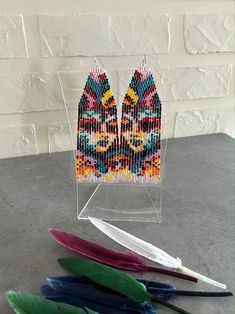 a pair of colorful beaded earrings sitting on top of a table next to feathers