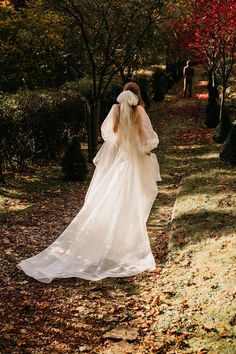 a woman in a wedding dress walking down a path with trees and leaves all around her