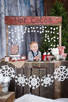 a little boy sitting at a table in front of a sign that says hot cocoa