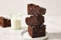 three pieces of chocolate cake on a white plate next to a glass of milk and another piece of brownie