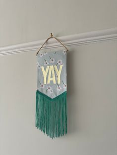 a wall hanging with the word yay on it and daisies in yellow letters