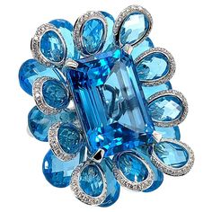 This ring features an exquisite 21.51 carat blue topaz as the center stone. This gorgeous gemstone is laid on top of a bed of luscious blue topaz briolettes to highlight the peaceful hue of the gems. The architectural layering of the floral blue topaz beds makes this piece mesmerizing to look at from any and every angle. Fancy blue topaz ring in 18K white gold with diamonds. Blue Topaz: 21.51 carat octagon shape - center stone. Blue Topaz: 37.57 carat pear briolettes - 20 pieces. Diamonds: 0.68 Exquisite Luxury Topaz Wedding Ring, Luxury Handmade Blue Topaz Jewelry, Luxury Hallmarked Blue Topaz Jewelry, Luxury White Topaz Jewelry With Gemstone Accents, Luxury Exquisite Blue Topaz Jewelry, Luxury Topaz Jewelry With Gemstone Accents, Ocean Queen, Topaz Cocktail Ring, Dear Ava