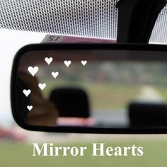 the reflection of two people in a car's rear view mirror with hearts drawn on it