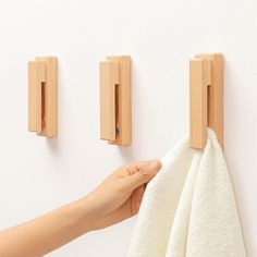 a hand holding a towel in front of two wooden hooks