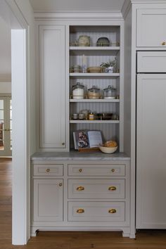 a kitchen with white cupboards and gold pulls on the doors, along with an open bookcase