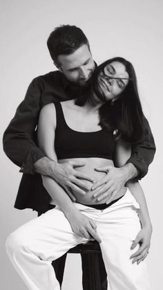 black and white photograph of a pregnant woman sitting on a man's lap with his arms around her belly