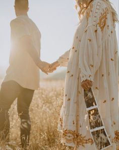 a man and woman holding hands while standing in a field with the sun behind them