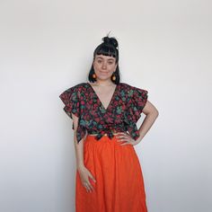 a woman standing in front of a white wall wearing an orange skirt and black top