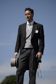 a man in a tuxedo holding a hat and camera while standing on top of a hill