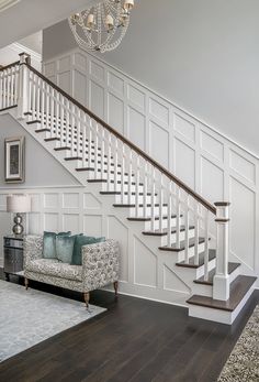 a living room filled with furniture and a chandelier hanging from the ceiling next to a stair case