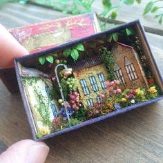 someone is holding a miniature house made out of tiny books and flowers in their hands