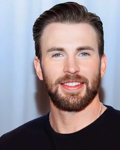 a close up of a person wearing a black shirt and beard smiling at the camera