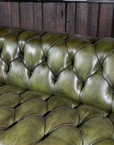 a green leather couch sitting in front of a wooden wall