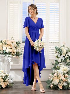 a woman standing in front of flowers wearing a blue dress and holding a white bouquet