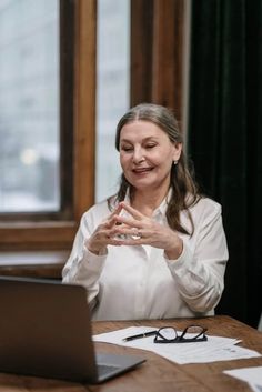 a woman sitting at a table in front of a laptop computer with her hands together