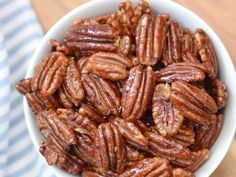 a white bowl filled with pecans sitting on top of a wooden table next to a blue and white towel