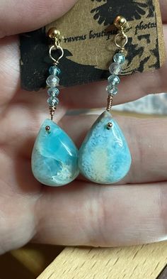 "Beautiful Larimar pear-shaped drops are the main focal bead of these elegant and summery gold-filled drop earrings. These genuine gems, a very specific natural form of blue chalcedony, are only found in the Dominican Republic. Notice that in natural light they appear light blue, and in artificial light they have a bit of a teal hue as well (see the pics). Silicon push-backs secure the gold-filled posts to your ear. Total length is ca. 1 1/4\" or 3.5 cm. The color of the stone is beautifully reminiscent of Caribbean seawater: paradoxically you should not leave Larimar gemstones in the sunlight as they will bleach, though. These teardrops have both wavy undulations in their colour, and the \"leopard spots\" characteristic of Larimar." Rose Gold Bangle, Artificial Light, Natural Form, Leopard Spots, The Dominican Republic, Blue Chalcedony, Gold Drop Earrings, Focal Bead, Dominican Republic