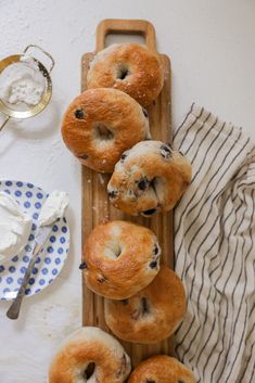 several bagels are arranged on a wooden tray next to a cloth and spoons