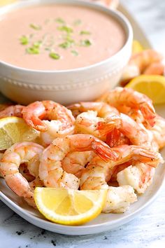 a plate with shrimp, lemon wedges and a bowl of soup on the side