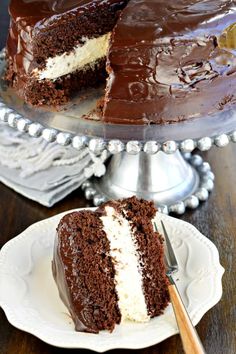 a chocolate cake with white frosting and one slice cut from it on a plate