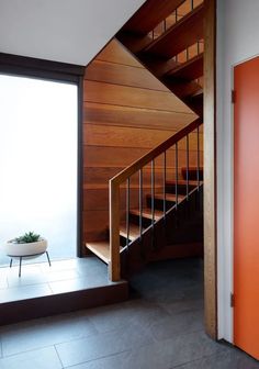 a stair case next to an orange door with a planter on the bottom floor